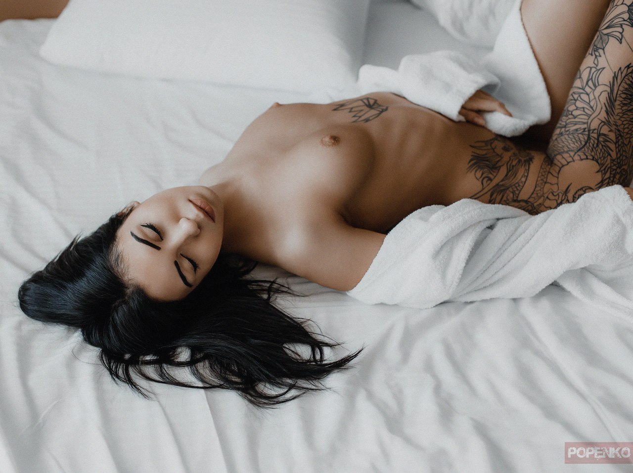 Девушка с татуировкой раздевается на постели 
