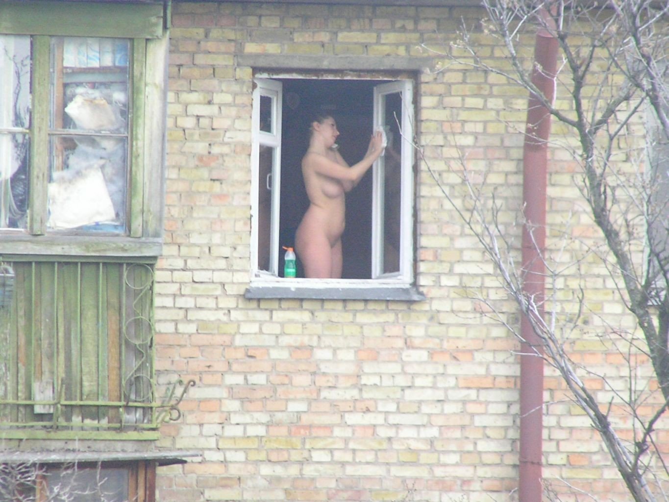 Молодая девушка позирует голая возле балконной двери